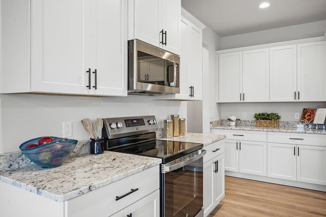 kitchen featuring light stone counters, light wood-style flooring, appliances with stainless steel finishes, and white cabinetry