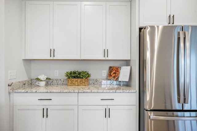 kitchen with light stone counters, white cabinets, and freestanding refrigerator