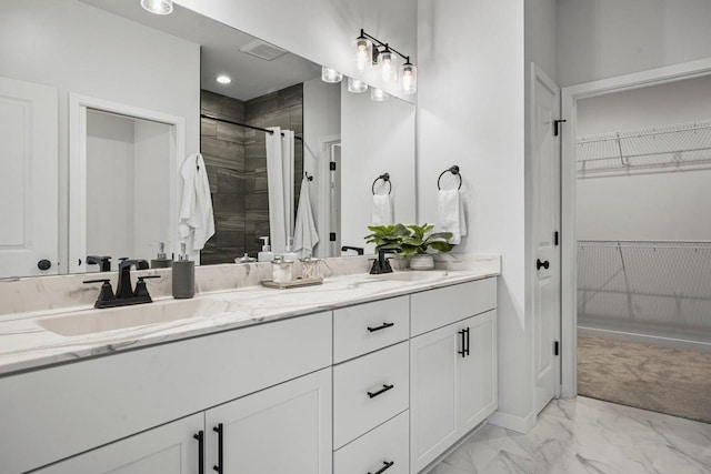 bathroom featuring marble finish floor, tiled shower, a walk in closet, and a sink