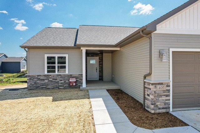 entrance to property with stone siding, board and batten siding, a shingled roof, and a garage