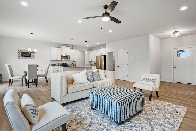 living room featuring recessed lighting, baseboards, light wood-style flooring, and ceiling fan with notable chandelier