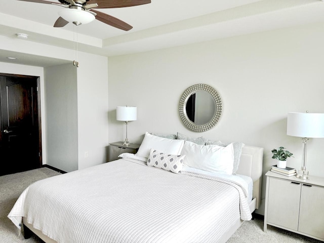 bedroom featuring a tray ceiling, light colored carpet, and ceiling fan