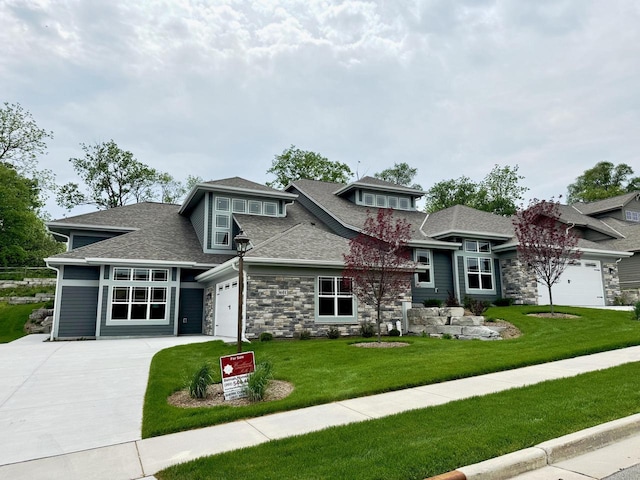 prairie-style house featuring a front yard, roof with shingles, a garage, stone siding, and driveway