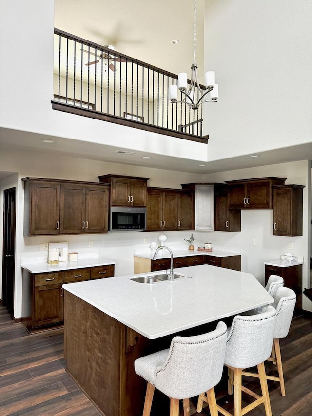 kitchen with a center island with sink, a sink, stainless steel microwave, dark wood finished floors, and dark brown cabinetry