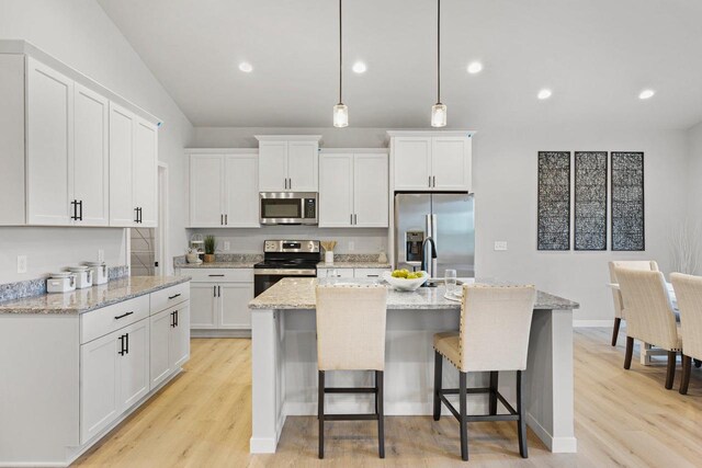 kitchen with a center island with sink, light wood finished floors, a breakfast bar, stainless steel appliances, and white cabinets