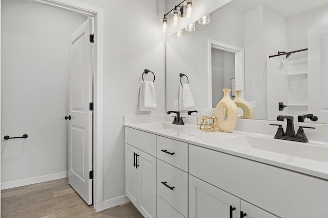 bathroom with a sink, baseboards, wood finished floors, and double vanity