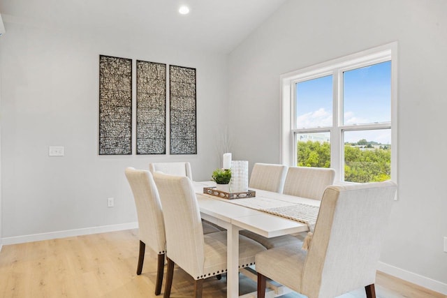dining area with baseboards, vaulted ceiling, and light wood finished floors
