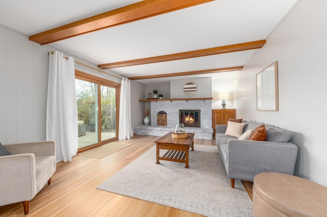 living room featuring beam ceiling, a brick fireplace, and light wood-style flooring