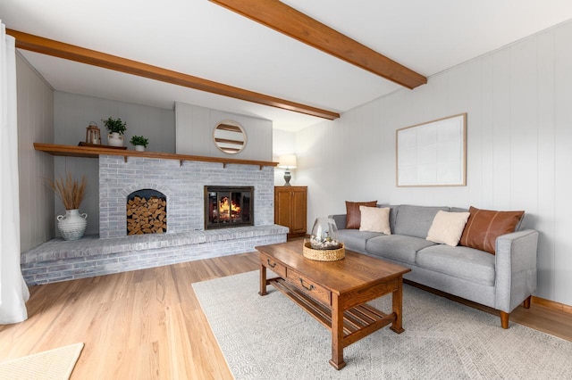 living area featuring light wood-type flooring, beam ceiling, and a fireplace