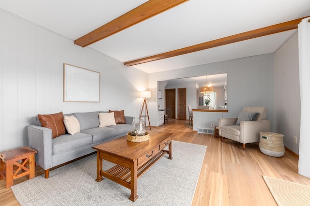 living area with beam ceiling, visible vents, and light wood-type flooring