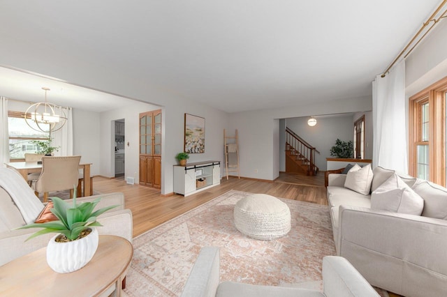 living area with stairway, baseboards, an inviting chandelier, and light wood-style flooring