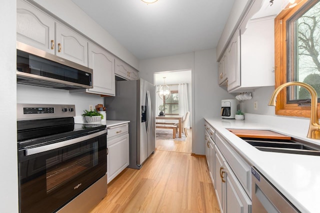 kitchen with light countertops, appliances with stainless steel finishes, light wood-style floors, a notable chandelier, and a sink