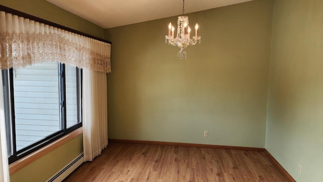 spare room with a baseboard radiator, baseboards, an inviting chandelier, and wood finished floors