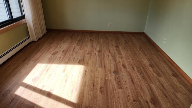 empty room featuring a baseboard radiator, baseboards, and wood finished floors