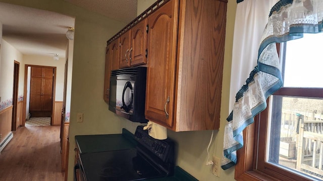 kitchen featuring range with electric cooktop, brown cabinets, black microwave, and wood finished floors