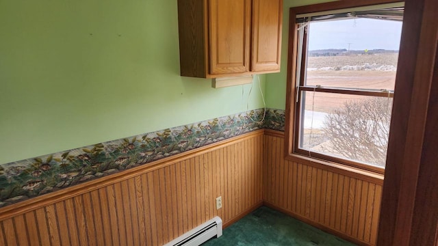 carpeted empty room featuring a wainscoted wall, baseboard heating, and wooden walls