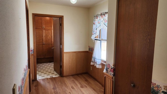 hall with light wood-style flooring, wooden walls, and wainscoting