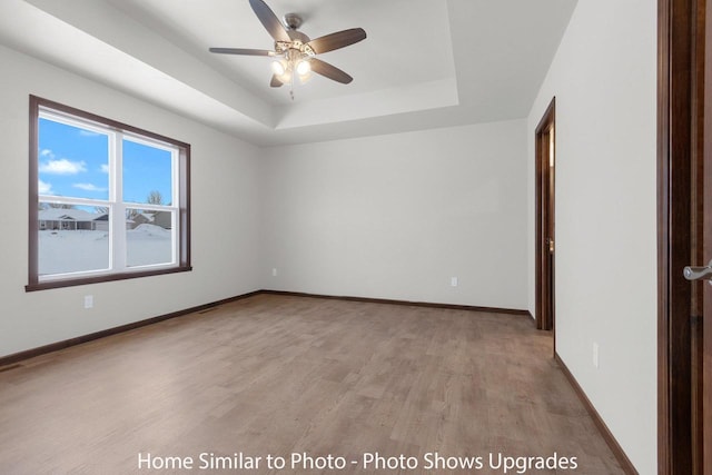 unfurnished room with a tray ceiling, baseboards, light wood-style flooring, and a ceiling fan