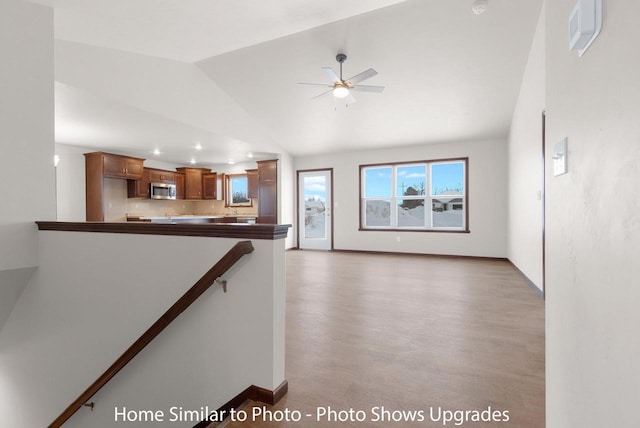 unfurnished living room with ceiling fan, baseboards, lofted ceiling, and wood finished floors