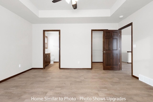 unfurnished bedroom with a walk in closet, a raised ceiling, and baseboards