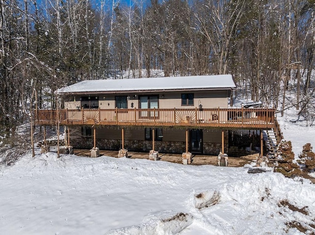 snow covered house with a wooden deck, stone siding, and stairs