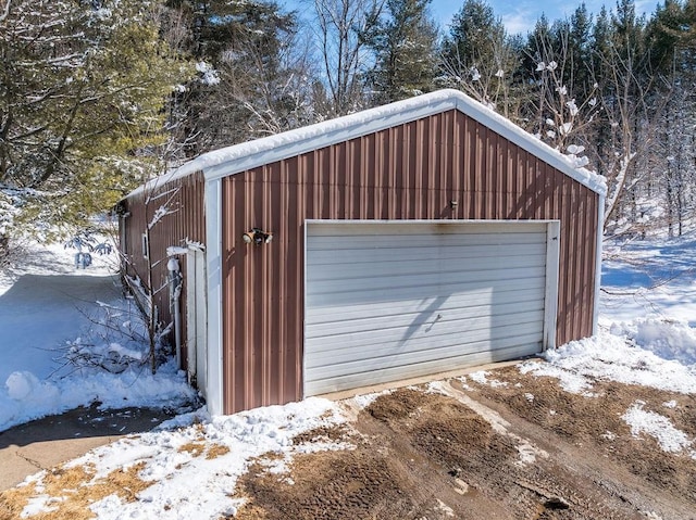 snow covered garage with a garage and dirt driveway