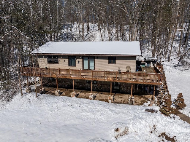 snow covered back of property with stairs and a deck