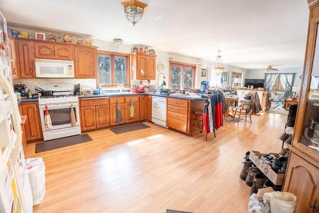 kitchen with brown cabinets, light wood-style flooring, open floor plan, white appliances, and a peninsula