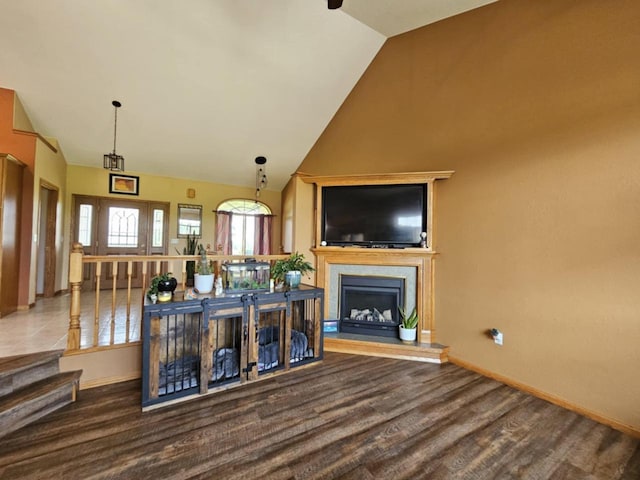 living room with wood finished floors, a fireplace with raised hearth, baseboards, and high vaulted ceiling