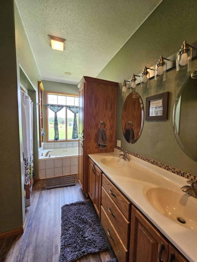 bathroom with a sink, a relaxing tiled tub, a textured ceiling, and wood finished floors