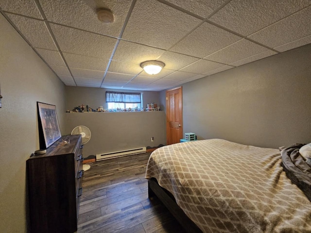 bedroom with a drop ceiling, a baseboard radiator, and dark wood-style floors