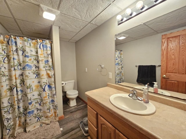 bathroom with toilet, curtained shower, wood finished floors, a paneled ceiling, and vanity