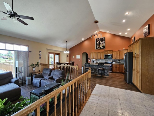 tiled living room with arched walkways, recessed lighting, ceiling fan with notable chandelier, and high vaulted ceiling