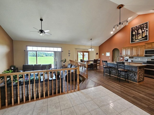 dining space with light tile patterned floors, arched walkways, high vaulted ceiling, and ceiling fan with notable chandelier