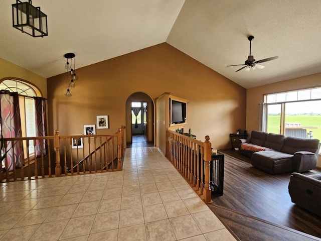 corridor featuring tile patterned flooring, an upstairs landing, arched walkways, and high vaulted ceiling