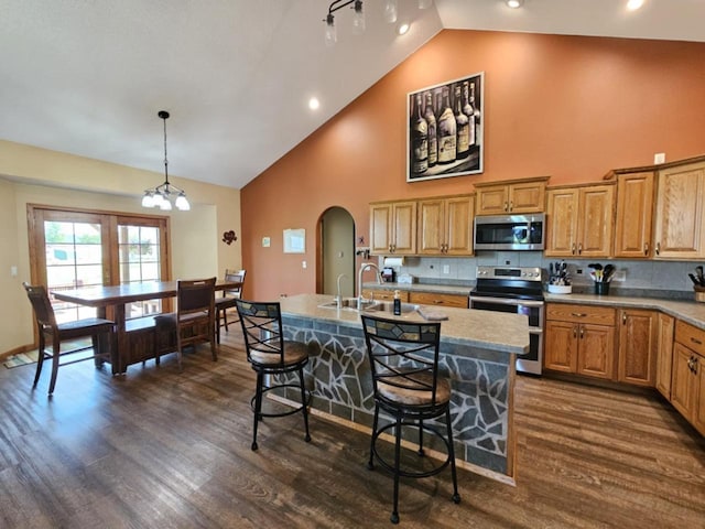 kitchen featuring a center island with sink, dark wood finished floors, stainless steel appliances, arched walkways, and a breakfast bar area