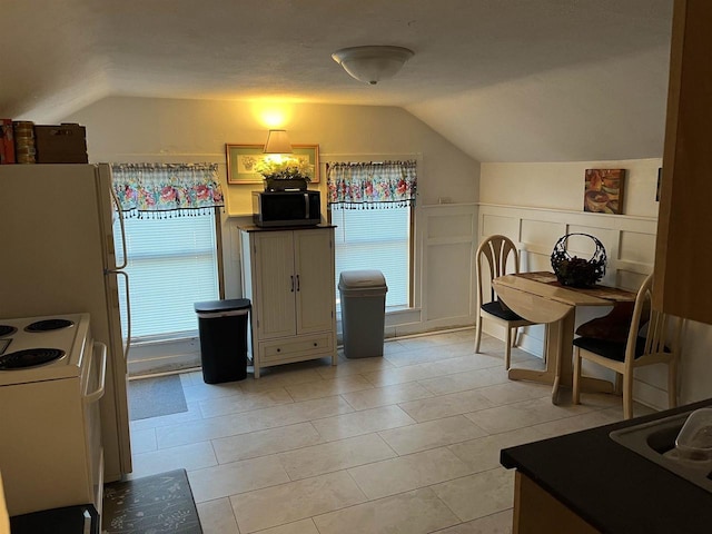 kitchen featuring vaulted ceiling, dark countertops, white electric range, and a wainscoted wall