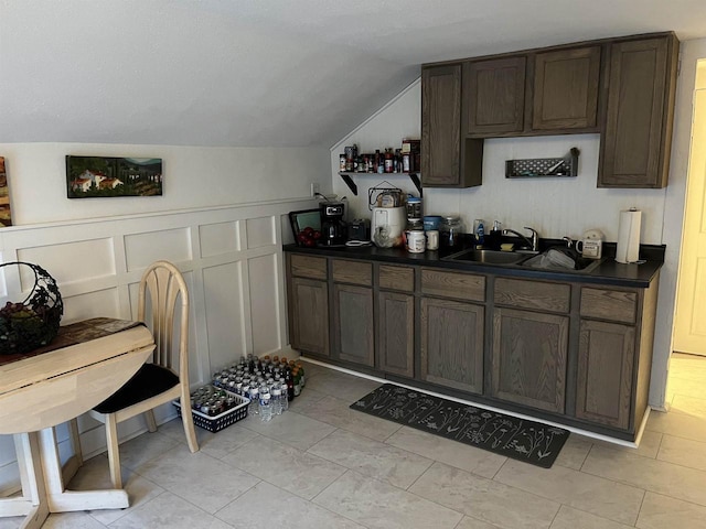 interior space featuring dark countertops, dark brown cabinetry, vaulted ceiling, a decorative wall, and a sink