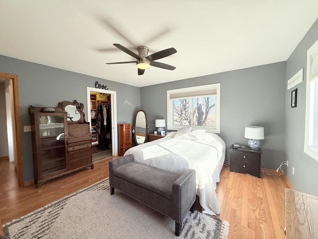 bedroom with a closet, a walk in closet, a ceiling fan, and wood finished floors