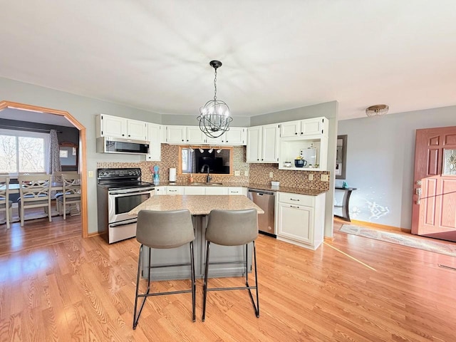 kitchen with light wood finished floors, a sink, decorative backsplash, appliances with stainless steel finishes, and a notable chandelier