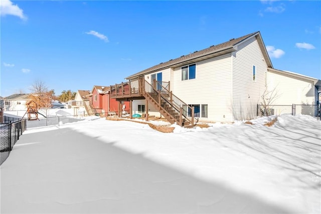 snow covered back of property featuring stairway, fence, a residential view, and a wooden deck