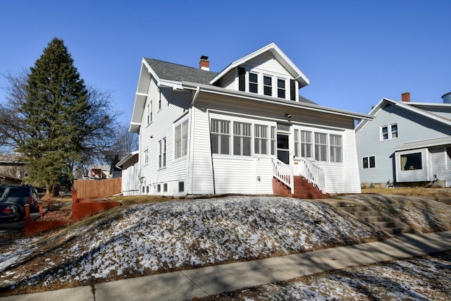 view of front of home featuring a shingled roof, a chimney, and a sunroom