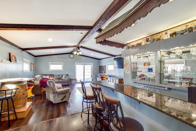 kitchen with dark stone counters, plenty of natural light, dark wood-type flooring, and vaulted ceiling with beams