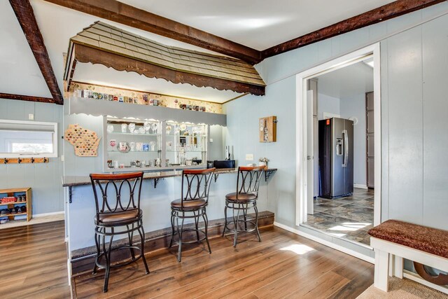 bar featuring wet bar, beam ceiling, wood finished floors, and stainless steel refrigerator with ice dispenser