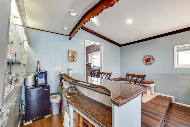 kitchen with a sink, refrigerator, dark wood finished floors, dark stone counters, and vaulted ceiling with beams