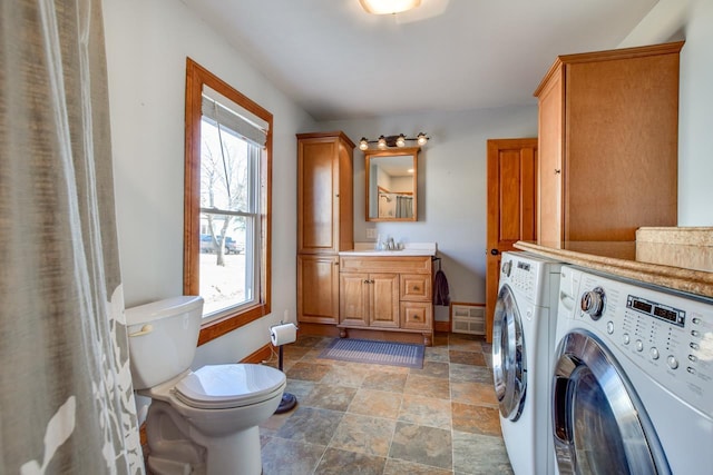 clothes washing area with baseboards, laundry area, washer and dryer, stone finish floor, and a sink