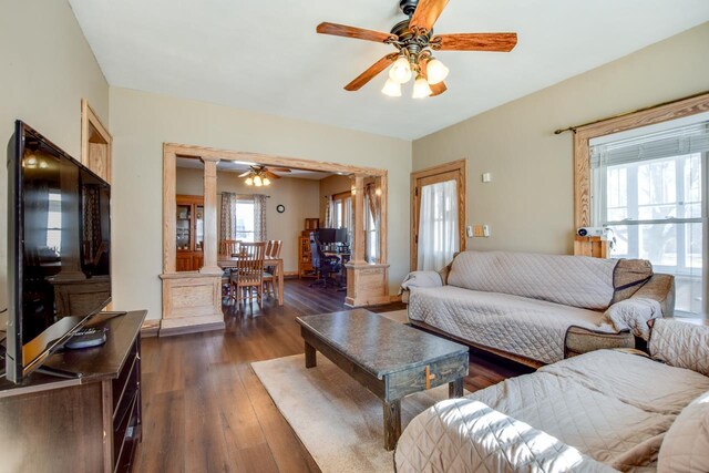 living area with dark wood-type flooring, a healthy amount of sunlight, ceiling fan, and ornate columns