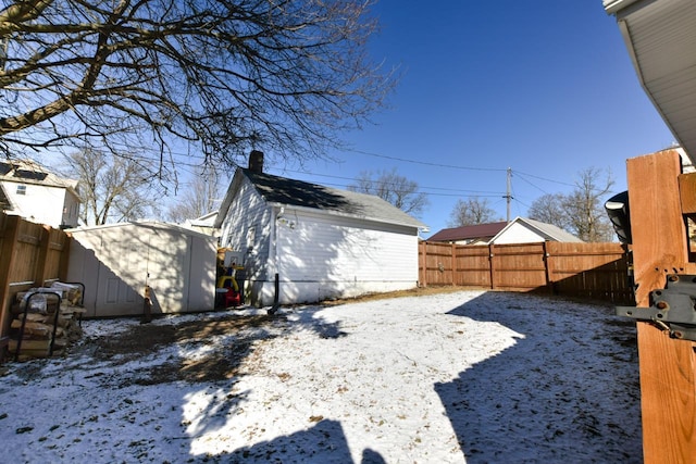 yard layered in snow with a storage unit, an outbuilding, and a fenced backyard