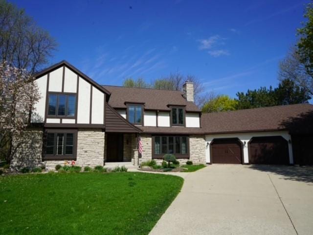 tudor house with a garage, stone siding, a front yard, and driveway