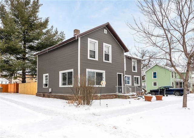 snow covered property featuring a chimney and fence